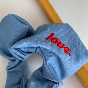 Detailed close-up of blue twill scrunchie with vivid red love embroidery decoration