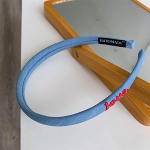 Detail of light blue fabric headband featuring red love embroidery and handmade label