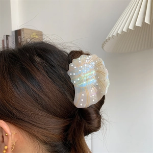 Iridescent shell-shaped acetate hair claw clip with gold accents on model's hair