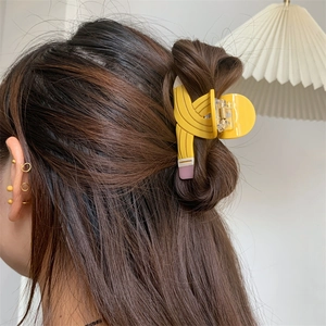 Detail view of a creative yellow pencil-shaped hair claw clip worn on long brown hair