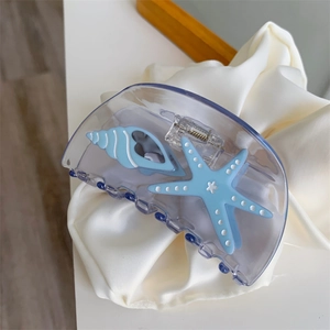 Detailed view of ocean-themed hair claw clip with starfish and seashell on silk fabric