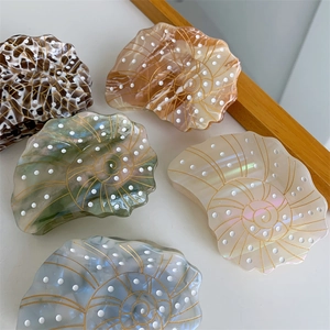 Detail of five marble-textured acetate hair claws in seashell shapes with gold spiral patterns
