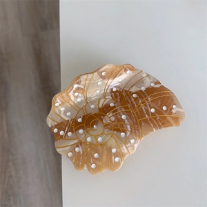Macro view of shell-shaped acetate hair claw with golden spiral lines and marble texture