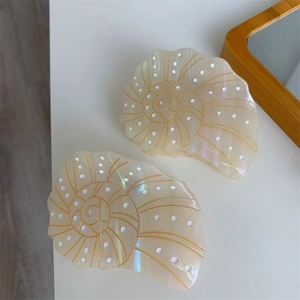 Detailed view of two pearlescent seashell hair claws with golden spiral lines on white desk