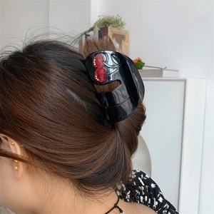 Detail of a large black acetate hair claw clip featuring red cherry accents and rhinestones