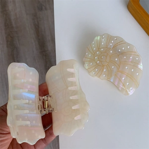 Detailed close-up of a pearlescent white seashell hair claw clip with golden spiral details