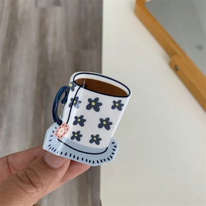 Detail of coffee cup shaped acrylic hair claw clip with blue floral patterns and pink tag