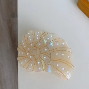 Detailed view of sea shell hair claw clip with pearlescent finish and golden spiral accents
