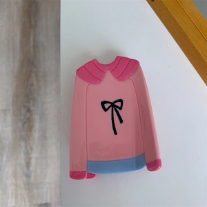 Détail d'une pince à cheveux rose en forme de pull avec un petit nœud noir élégant