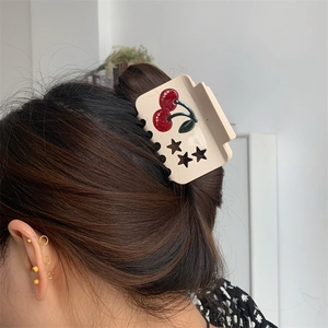 Detail view of acetate cherry hair claw clip with rhinestones worn on a woman's hair