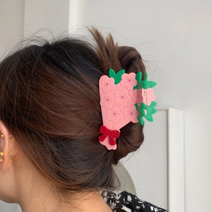 Détail d'une pince à cheveux fleur rose avec feuilles vertes et nœud rouge sur modèle