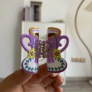 Detailed view of cup-shaped acrylic hair claw with purple floral patterns and yellow tea bag motifs