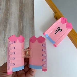 Détail d'une pince à cheveux rose en forme de pull avec nœud noir et finition résine