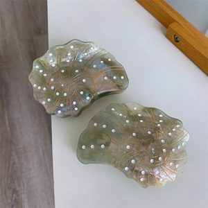 Detail view of two sea shell acetate hair claws in iridescent green with gold accents