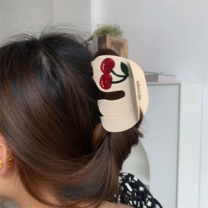 Detail view of large acetate hair claw clip with red cherry design on a French bun