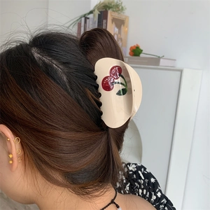 Detailed view of beige acetic acid hair claw with red cherry design on a hairstyle