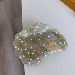 Close-up of ocean-themed conch hair claw in pearl finish with marble texture and gold lines