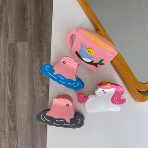 Detailed view of four unique acetate hair claw clips featuring dolphin and unicorn designs