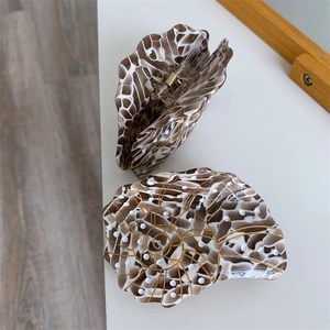 Detail of seashell-shaped acetate hair claws with marble texture and gold spiral lines