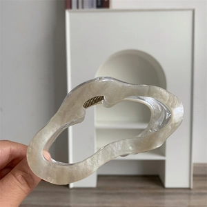 Détail d'une pince à cheveux ondulée crème nacrée avec finition brillante et ressort