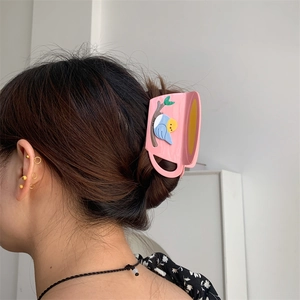 Pink coffee cup hair claw clip with a 3D blue bird design worn on hair from a side view