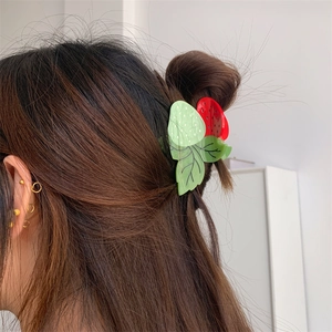 Détail d'une pince à cheveux en forme de fraise rouge avec feuilles vertes sur un chignon