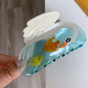 Detailed view of acetic acid swan hair claw with translucent blue water and fish design