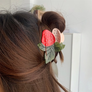 Détail de la pince à cheveux fraise en acétate sur un chignon de cheveux bruns