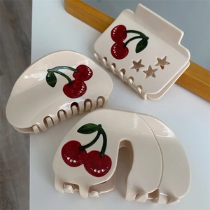 Detailed view of acetate cherry hair claws with red fruit patterns and sparkling rhinestones