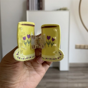 Detail view of a yellow boot-shaped hair claw with purple tulip patterns and metal spring