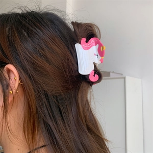 Close-up of a pink and white unicorn hair claw clip styled in a woman's hair bun