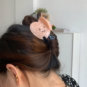 Dettaglio di una pinza per capelli in acetato rosa a forma di cuore con faccina sorridente