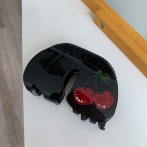 Detail of black acetate hair claw clip featuring red cherry design and small rhinestones