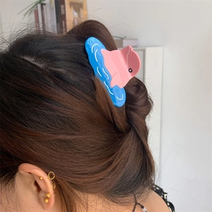 Close-up of a pink dolphin hair claw clip with blue waves styled on brown hair