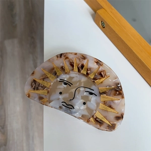 Detailed view of acetate hair claw clip featuring artistic sun face and golden rays