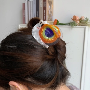 Détail de la pince à cheveux en forme d'escargot en acétate coloré sur un chignon