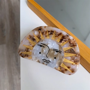 Detail view of acetate sun face hair claw clip with marble texture and golden rays
