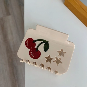 Detail view of cream acetate hair claw with red cherry design and sparkling rhinestones
