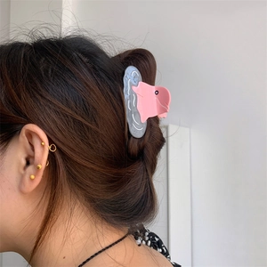 Pink blobfish shaped acetate hair claw clip worn on dark long hair in a close-up detail shot