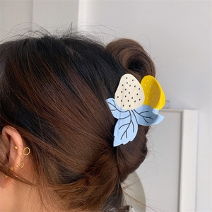 Détail de la pince à cheveux fraise avec feuilles bleues sur longs cheveux bruns naturels