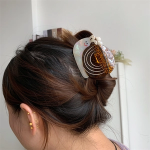 Détail d'une pince à cheveux en forme d'escargot en acétate avec perle sur femme