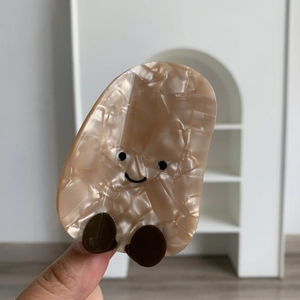 Dettaglio molletta per capelli in acetato beige con faccina e trama effetto marmo