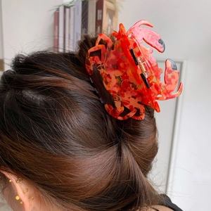 Détail d'une pince à cheveux crabe orange avec motifs écailles de tortue sur cheveux bruns