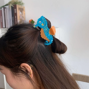 Detail of a blue seahorse hair claw clip with orange fins styled in a ponytail