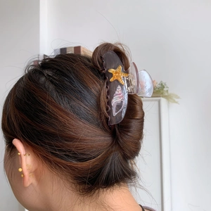 Detail view of acetate starfish hair claw clip worn on hair with minimalist earrings