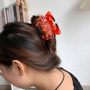 Détail d'une pince à cheveux crabe en acétate marbré rouge portée par un mannequin