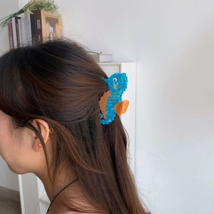 Blue seahorse acetate hair claw clip with orange accents worn in a half-up hairstyle