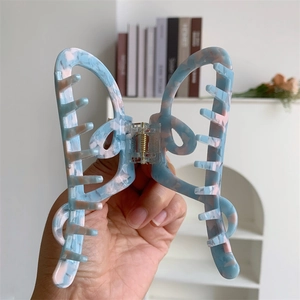 Detail of butterfly hair claw with blue pink marble texture held by hand in a cozy room