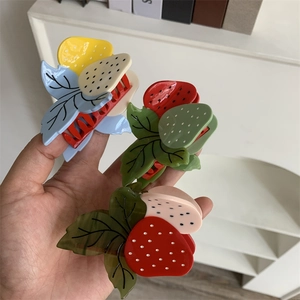 Détail des pinces à cheveux fraise et fruit du dragon en acétate tenues à la main