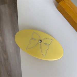 Detail of yellow oval hair clip featuring a sparkling rhinestone butterfly pattern